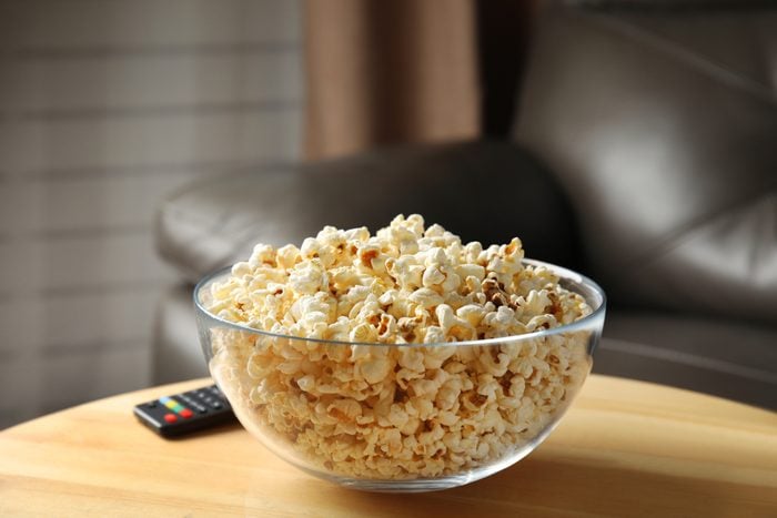 Bowl of popcorn and TV remote on table against blurred background. Watching cinema