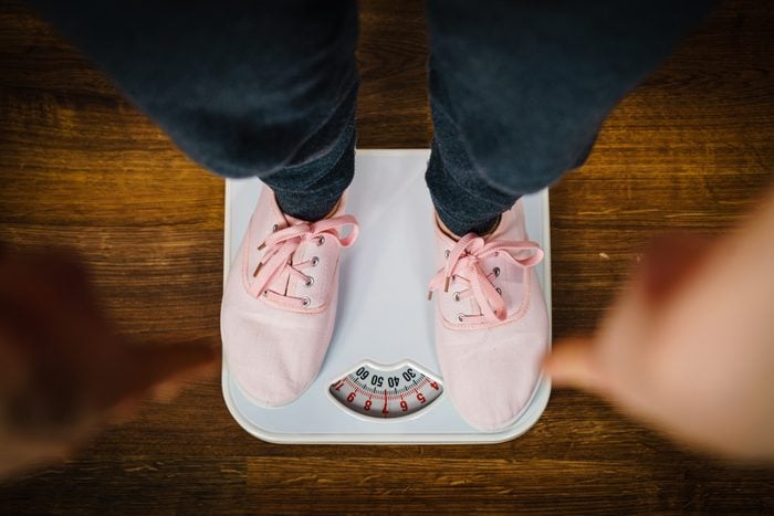 Bovenaanzicht van vrouwenvoeten die roze sneakers dragen op de weegschaal van de badkamer.  Fit, dieet, vetverlies concept.