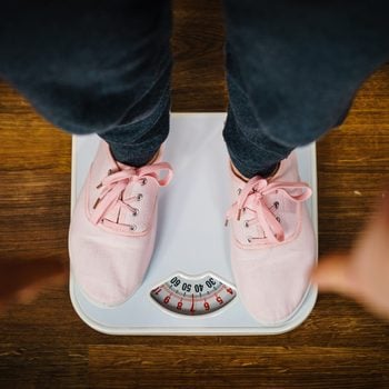 Top view of woman feet wearing pink sneakers on bathroom weight scale. Fit, dieting, fat loss concept.