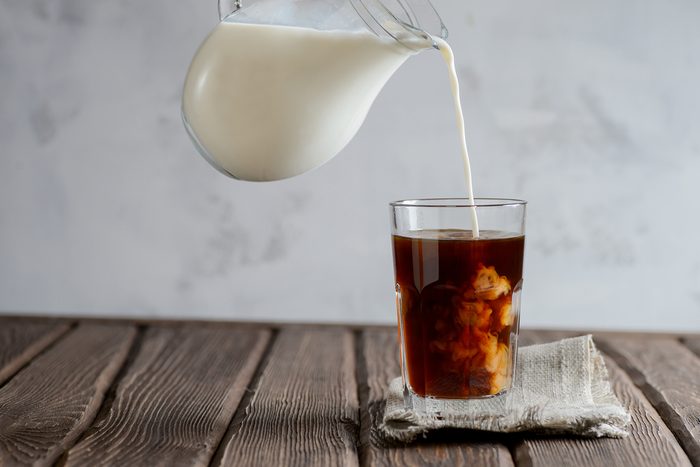 Iced coffee with pouring milk in glass on a wooden background