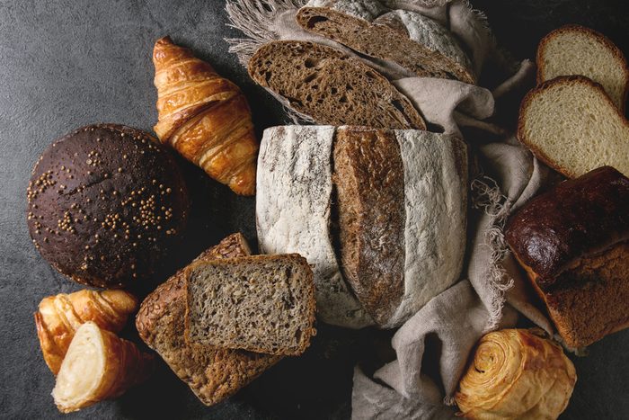 Variety of fresh baked rye, spelled, wheat craft artisan bread, whole and sliced, on cloth over black texture background. Flat lay, space