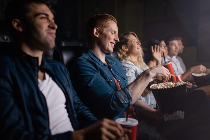 Young man with friends watching movie in cinema. Group of people in theater with popcorn and drinks.