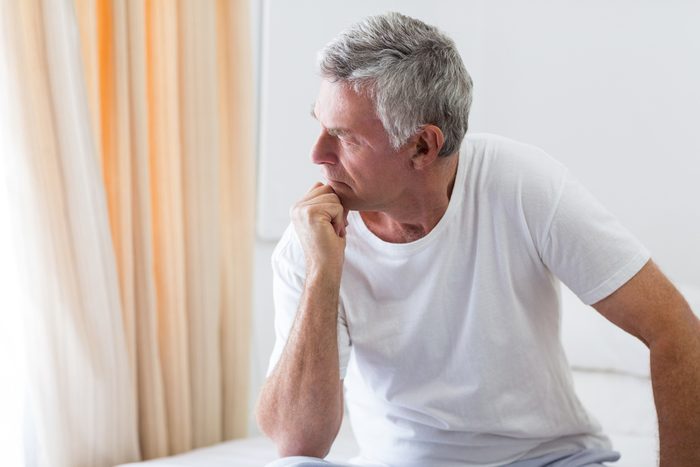 Worried senior man sitting on bed at home