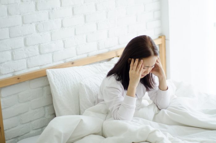 Asian women are headache severely.Lady wake up in the morning with migraine.Insomnia results in headaches when awakened.Young girl sitting on a stressed bed. In her bedroom.She was sick.