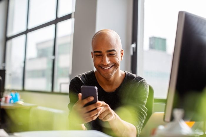 man at work looking at smartphone and smiling