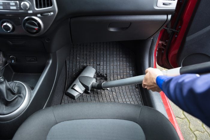 A person vacuuming a car mat with a vacuum cleaner.