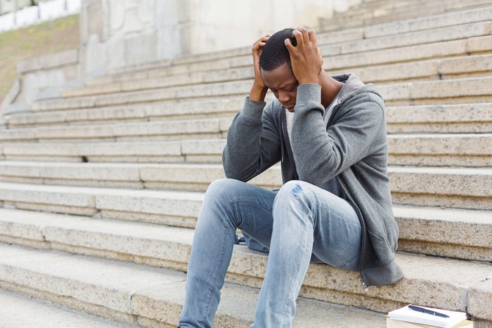 Stressed african-american man sitting alone with headache at university on stairs. Black depressed student guy failed exams, expelled from college, copy space