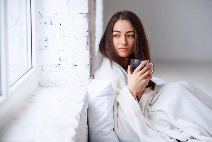 Young woman sipping coffee in bed, looking pensive