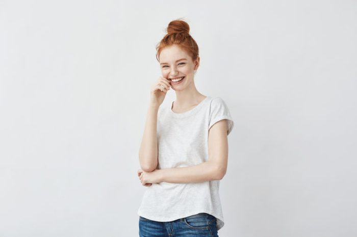 Portrait of young stylish freckled girl laughing with hand on cheek looking at camera. Copy space. Isolated on white