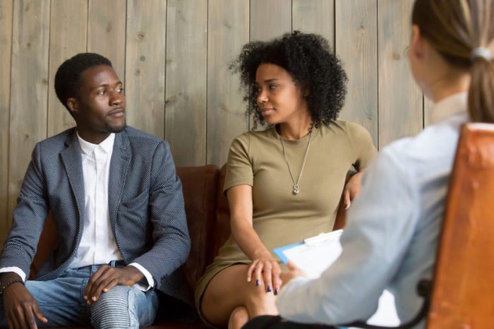 Reconciled black husband and wife looking at each other after successful psychological treatment from relationship counselor, African spouses make peace at therapy session, lovers ready to compromise