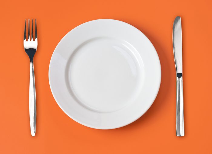 Knife, white plate and fork on orange background