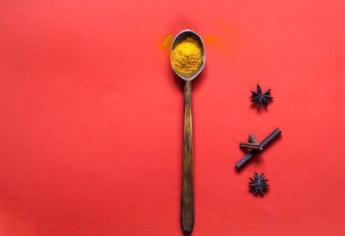 Wooden spoon with turmeric and spices on the background of living coral. The trend colour of the year 2019. Copy space, closeup