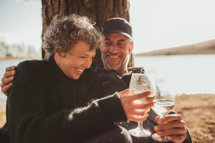 Portrait of relaxed mature couple having a glass of wine at campsite. Senior man and woman toasting wine at on summer day.