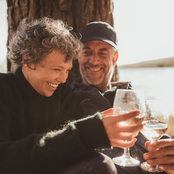 Portrait of relaxed mature couple having a glass of wine at campsite. Senior man and woman toasting wine at on summer day.