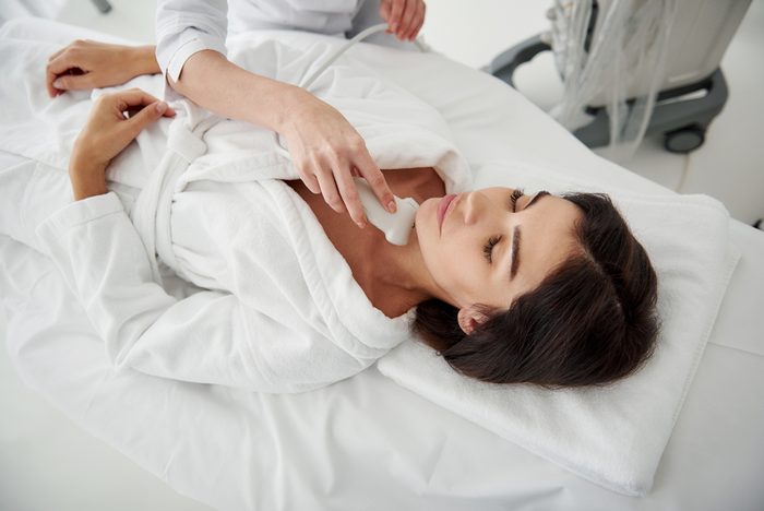 Portrait of beautiful lady in white bathrobe having ultrasound scanning of thyroid