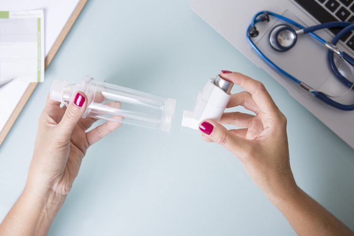 Top view of a close up of the hands of a female doctor is inserting a pressurized cartridge inhaler into an inhalation chamber on a medical demonstration on her desk 