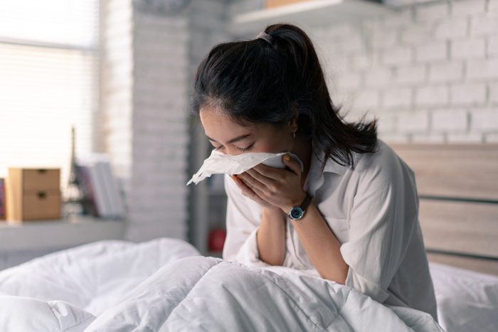 Asian woman in bed, sneezing into a tissue
