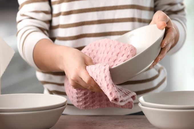 Woman wiping dishware with cotton towel in kitchen.
