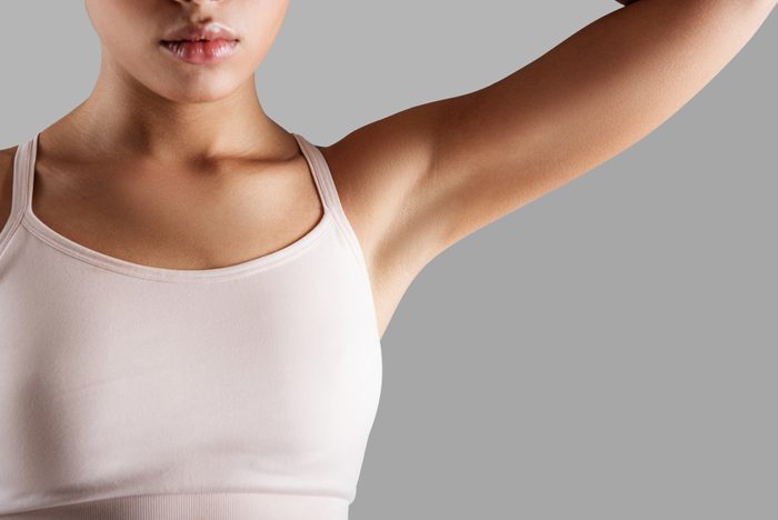 Close up of woman torso in close fitting brassiere. Her face expressing tranquility. Girl is showing her armpit. Isolated on background