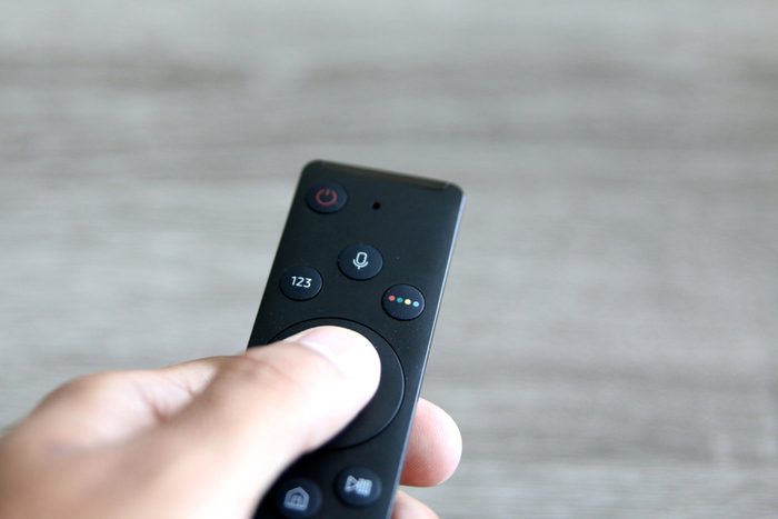 hand pressing remote control over a light grey background