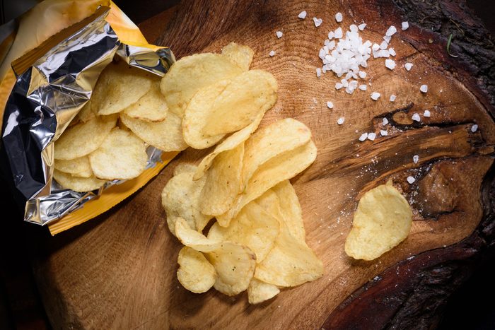 Snack of potato chips with sea salt over wooden background. Top view.