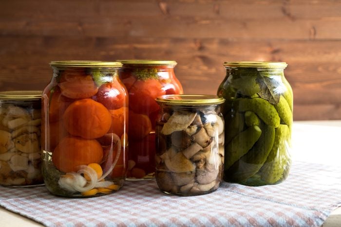 Marinated cucumbers, tomatoes and mushrooms in glass jars on the table.