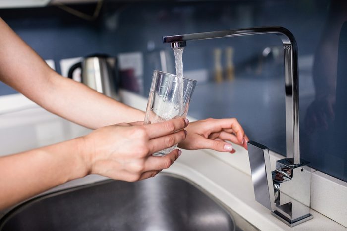 Cropped image of woman filling water in glass from faucet at kitchen sink