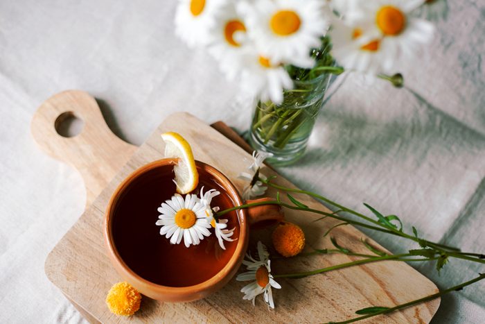 Herbal tea with fresh chamomile flowers in a ceramic mug on a linen tablecloth