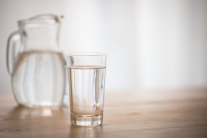 glass of water on a wooden table with a pitcher out of focus in the background