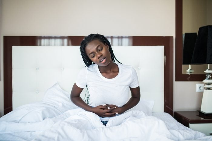 Young african woman suffering from stomach pain lying on bed at home