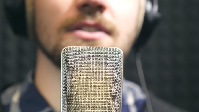 Young man emotionally recording new song. Working of creative musician. Male singer in headphones singing song into the microphone at sound studio. Show business concept. Slow motion Close up.