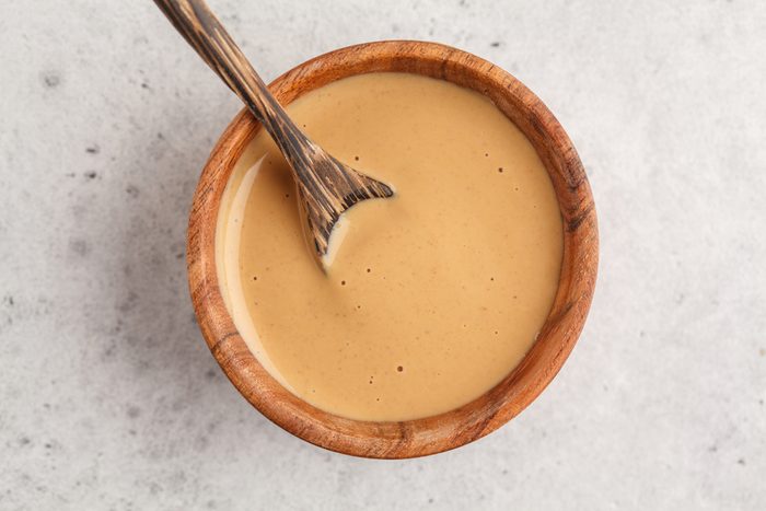 Creamy homemade peanut butter in a wooden bowl, top view. Healthy vegan food concept.