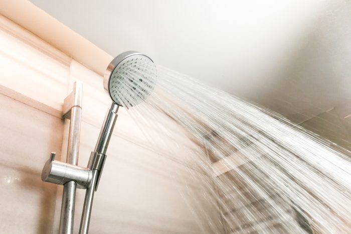 Shower head with refreshing water droplets spraying down in bathroom