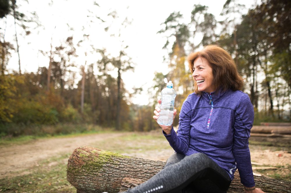 Senior runner sitting on wooden logs, resting, drinking water.
