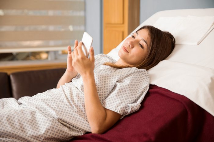 young woman in hospital bed using cell phone