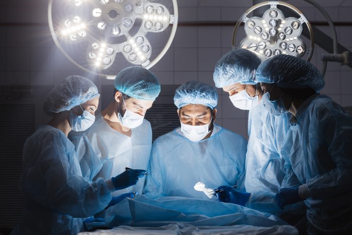 Shot of a multiracial surgeon team consists of trained surgeons, trauma specialists and plastic surgeons, consulting during difficult operation proceed, standing before unconscious patient in O.R.