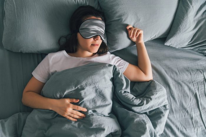 Mujer durmiendo en un parche en el ojo en una cama gris.  copie el espacio