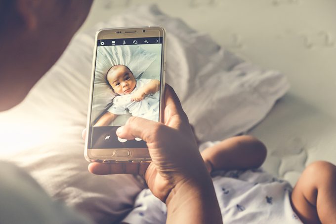 High angle shot of happy mother taking picture her baby boy in bed with smart phone at home.