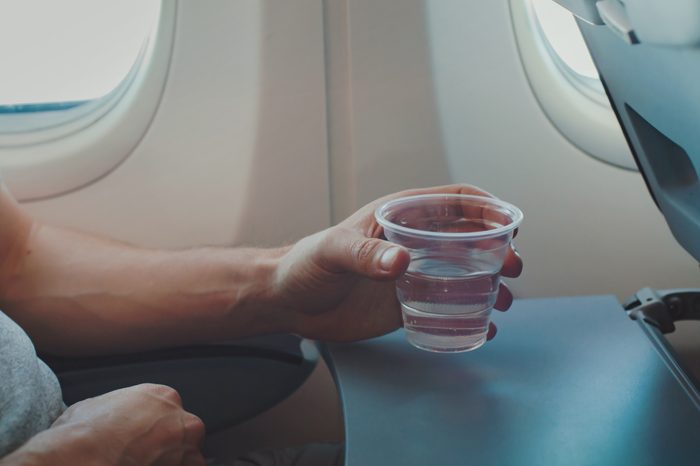 Passenger drinking water in airplane during flight. Close up of hand holding glass in plane.