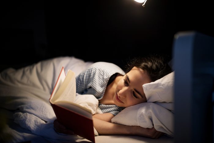 woman laying in bed at night reading a book