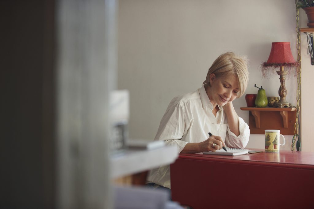 older woman writing in journal at desk