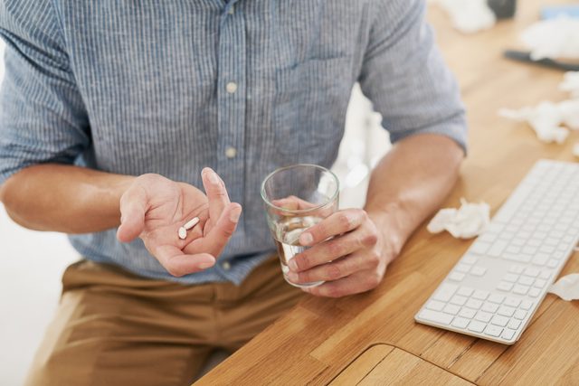 man holding a glass of water and two white pills