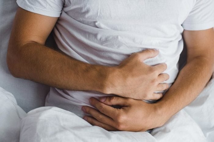 Man holding his stomach as if having abdominal cramps.