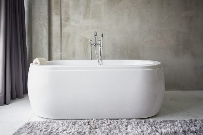 Big white bathtub in a middle of industrial loft bathroom style with grunge cement wall.
