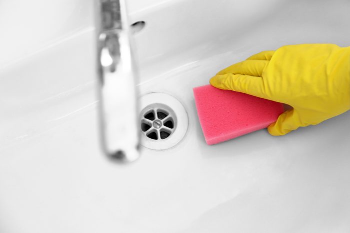 Female hand with sponge cleaning a sink in the bathroom