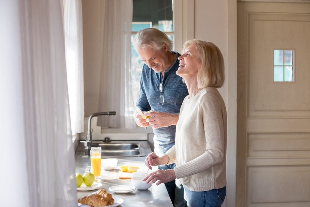 Happy loving senior couple having fun preparing healthy food on breakfast in the kitchen, mature smiling man and woman laughing cooking together on weekend morning, aged old family at home concept|