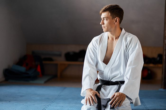 Karate do man in kimono sits on knees on floor in martial arts gym