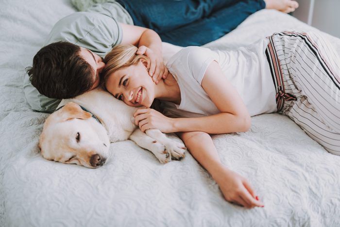 Pleasant young couple having rest in bed while their dog sleeping nearby