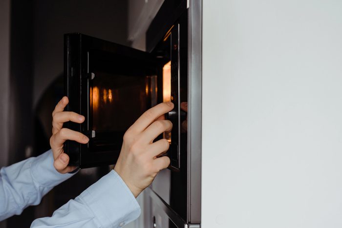 A man dressed in a business shirt puts a dish into the microwave oven. 
