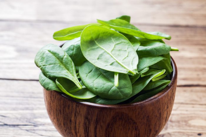 Fresh spinach leaves in bowl on rustic wooden table